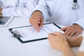 Doctor and patient talking while sitting at the desk in office. Physician pointing into medical history form. Medicin Royalty Free Stock Photo