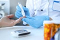 Doctor piercing patients finger with lancet in clinic closeup