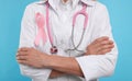 Doctor with pink ribbon and stethoscope on light blue background, closeup. Breast cancer awareness Royalty Free Stock Photo