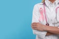 Doctor with pink ribbon and stethoscope on light blue background, closeup and space for text. Breast cancer awareness Royalty Free Stock Photo