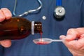 A doctor pours medicine from a bottle into a plastic spoon prior to administering it to a patient.