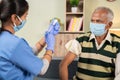 Doctor preparing vaccination shot to elderly patient by holding syringe at home - concept of home health check to