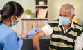 Doctor preparing vaccination shot to elderly patient by holding syringe at home - concept of home health check to