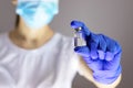 Doctor in protective gloves and mask holding glass vial with injection liquid. Vaccination against influenza and coronavirus.