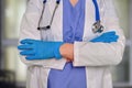 A doctor in protective gloves with a stethoscope stands with his arms Royalty Free Stock Photo