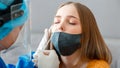 Doctor in protective medical mask taking PCR test nasopharyngeal culture to woman. Diagnostics testing patients coronavirus covid