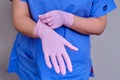 The doctor puts on pink protective gloves, close-up. Hands of a medic in a blue uniform