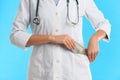 Doctor putting bribe money into pocket on blue background, closeup. Corruption in medicine Royalty Free Stock Photo