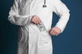 Doctor putting bribe in pocket on color background. Corruption concept Royalty Free Stock Photo