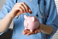 Doctor putting coin into piggy bank, closeup. Medical insurance