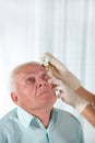 Doctor putting drops into a senior man's eyes