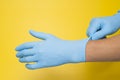 Doctor putting on protective blue gloves isolated on yellow background