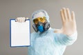 A doctor in a respirator and protective clothing shows a stop sign with his palm and holds a paper with a diagnosis