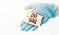 Doctor\'s hand in blue glove shows the wooden cubes with text LIFE LONG. Medical concept