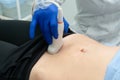 Doctor`s hand moves ultrasound sensor on pregnant woman`s stomach in hospital