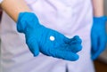 A doctor`s hand, a nurse in a blue latex glove gives a pill lying on the palm of her hand. A female doctor in a blue rubber glove