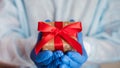 Doctor`s hands in medical gloves holds a gift box with a red ribbon. Clse-up Royalty Free Stock Photo