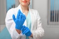 Doctor`s hands putting on latex gloves in a hospital. Woman in a doctor`s smock in latex gloves. Protection against