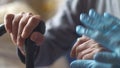 Doctor`s hands in rubber gloves hold and hug the hand of an elderly man with a cane walking stick. Rehabilitation of a sick pensio