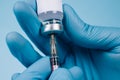 Doctor or scientist holding vial dose of common vaccine with syringe against blue background with copy space - global vaccination