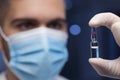 Doctor or scientist with medical mask holding a ampule with vaccine in his hand