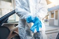 Doctor, scientist or nurse wearing face mask and biological hazmat protective suit putting on rubber gloves near car outdoor.