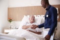 Doctor Shaking Hands With Senior Male Patient In Hospital Bed In Geriatric Unit