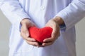 Doctor showing compassion and support holding red heart onto his chest in his coat.