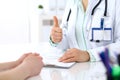 Doctor showing Ok sign with thumb up to patient while sitting at the desk in hospital office, close-up of human hands