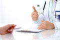 Doctor showing Ok sign with thumb up to patient while sitting at the desk in hospital office, close-up of human hands