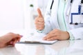 Doctor showing Ok sign with thumb up to patient while sitting at the desk in hospital office, close-up of human hands