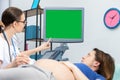 A doctor shows a pregnant patient her unborn baby on an ultrasound screen. Green screen. Gynecology office. Royalty Free Stock Photo