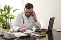 The doctor sits at his desk, taking notes talking on the phone.