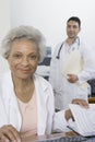 Doctor Sitting With Documents And Colleague Standing In Background Royalty Free Stock Photo