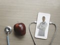 Doctor on smartphone screen, stethoscope and red apple on table, doctor online concept, online medical communication and medical