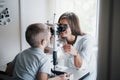 Doctor is smiling. Little boy having test for his eyes with special optical apparatus by female doctor