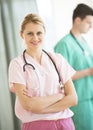 Doctor Standing Arms Crossed With Colleague In Background At Clinic Royalty Free Stock Photo