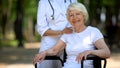 Doctor standing behind handicapped elderly woman, looking at camera, support