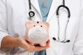 Doctor with Stethoscope Holding Piggy Bank Wearing Medical Face Mask