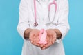 Doctor with stethoscope holding pink ribbon on light blue background, closeup. Breast cancer awareness Royalty Free Stock Photo