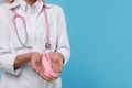 Doctor with stethoscope holding pink ribbon on light blue background, closeup and space for text. Breast cancer awareness Royalty Free Stock Photo