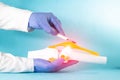 Doctor surgeon holds a scalpel near the knee joint mockup on a blue background. The concept of joint replacement surgery,