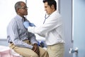 Doctor In Surgery Listening To Male Patient's Chest