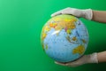 Doctor in surgical gloves holding globe against green background, closeup. Space for text Royalty Free Stock Photo