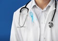 Doctor with symbolic blue ribbon on color background, closeup. Prostate cancer concept