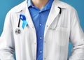 Doctor with symbolic blue ribbon on color background. Prostate cancer concept