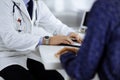 A doctor is talking to his patient, while sitting together at the desk in the cabinet in a hospital. Physician using Royalty Free Stock Photo