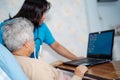 Doctor teach and suggest Asian senior or elderly old lady woman patient to using notebook computer while sitting on bed in nursing Royalty Free Stock Photo