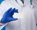 Doctor therapist is dressed in a white robe uniform and blue sterile gloves is standing and holding a stack of empty white paper