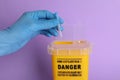 Doctor throwing used syringe needle into sharps container on violet background, closeup Royalty Free Stock Photo